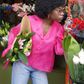 Afro-amerikanische junge Frau mit einem Blumenstrauß in der Hand, während Sie eine blaue Jeans an hat und eine Seiden Organza Bluse in Hot Pink von Lola Tong.